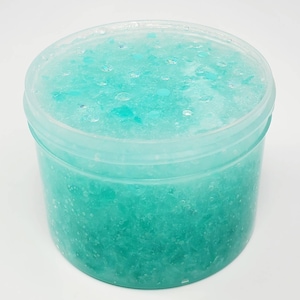 May include: A clear plastic container filled with light blue slime with white and blue glitter. The slime is thick and gooey and has a sparkly appearance.