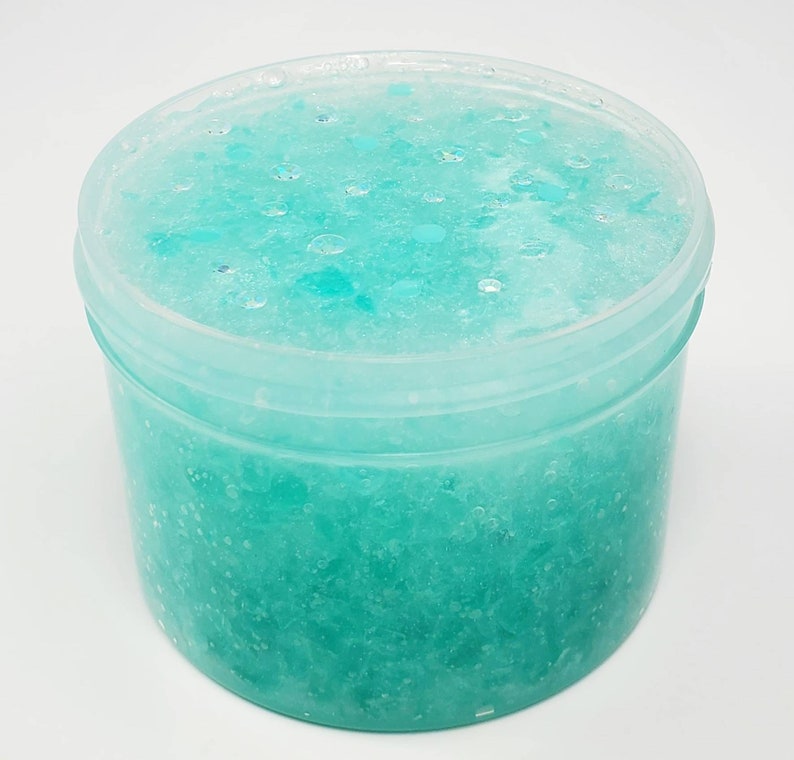 May include: A clear plastic container filled with light blue slime with white and blue glitter. The slime is thick and gooey and has a sparkly appearance.