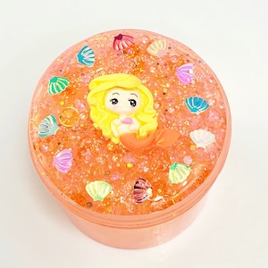 May include: Orange slime with glitter and a mermaid figurine inside a clear plastic container.