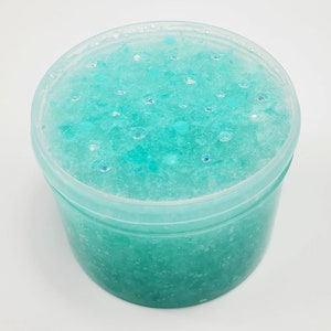 May include: A clear plastic container filled with teal blue slime with iridescent glitter.