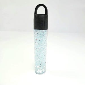 May include: A clear plastic tube with a black lid and a loop handle. The tube is filled with a clear liquid and silver glitter.