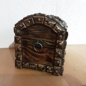 May include: A wooden treasure chest with a hinged lid and a metal latch. The chest is decorated with metal studs and has a dark brown finish.