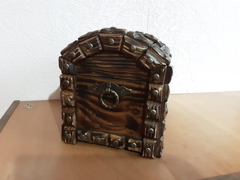 May include: A wooden treasure chest with a hinged lid and a metal latch. The chest is decorated with metal studs and has a dark brown finish.