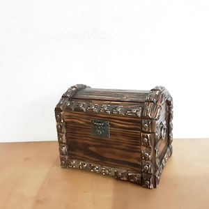 May include: A wooden treasure chest with a hinged lid and ornate metal accents. The chest is dark brown with a wood grain pattern.