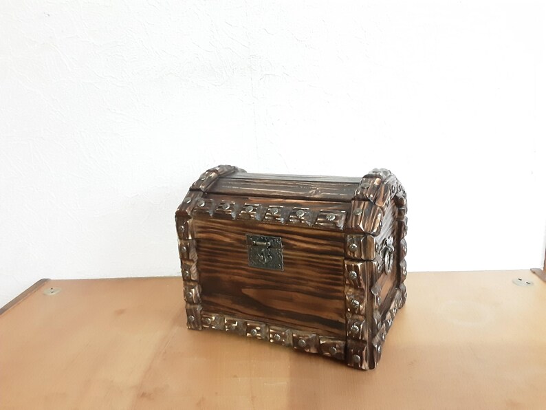 May include: A wooden treasure chest with a hinged lid and ornate metal accents. The chest is dark brown with a wood grain pattern.