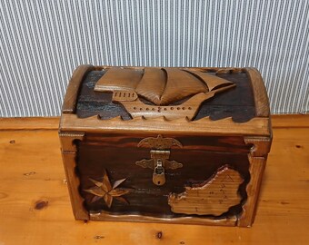 May include: A wooden treasure chest with a carved ship design on the lid. The chest is brown with a dark brown interior and features a star and map design on the front. It has a metal clasp and lock.