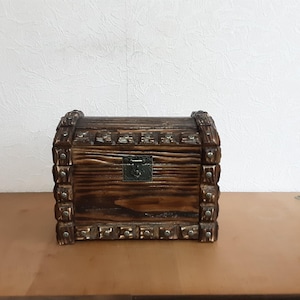 May include: A wooden treasure chest with a hinged lid and a metal latch. The chest is decorated with metal studs and has a dark brown finish.