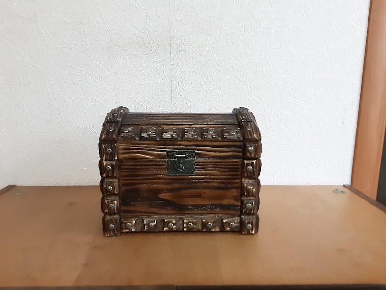 May include: A wooden treasure chest with a hinged lid and a metal latch. The chest is decorated with metal studs and has a dark brown finish.