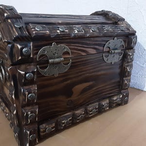 May include: A dark brown wooden treasure chest with metal hinges and decorative studs. The chest is closed and has a rustic, antique look.