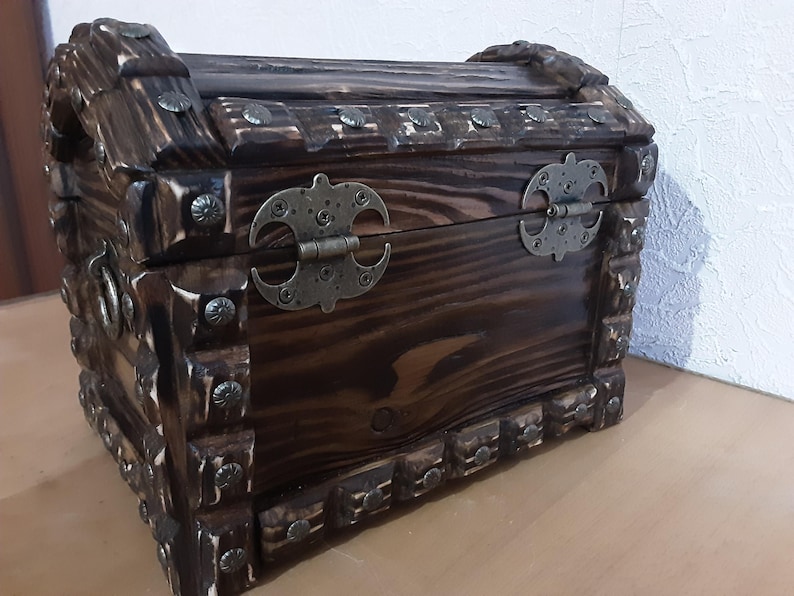 May include: A dark brown wooden treasure chest with metal hinges and decorative studs. The chest is closed and has a rustic, antique look.