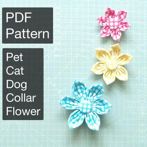 Op de afbeelding: Drie stoffen bloemversieringen in roze, geel en blauw met witte stippen. De bloemen zijn gerangschikt op een lichtblauwe rasterachtergrond. De tekst links luidt "PDF Pattern" en "Pet Cat Dog Collar Flower".