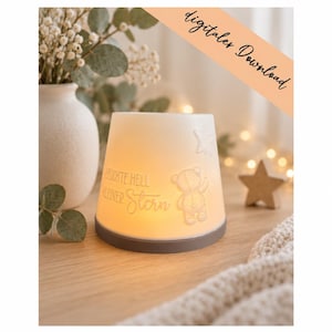 Könnte beinhalten: Eine weiße, konische, beleuchtete Lampe mit einem Relief eines Teddybären, der einen Stern hält, und dem Text "LEUCHTE HELL KLEINER Stern". Die Lampe hat einen soliden grauen Sockel und strahlt ein warmes, sanftes Licht aus ihrem Körper aus.