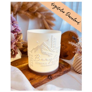 May include: A cylindrical, off-white candle holder with a mountain design and the word "Berglis" etched into the side. The words "Natur", "Auszeit", and "Leidenschaft" are also visible. The words "digitaler Download" are written on a diagonal orange banner.