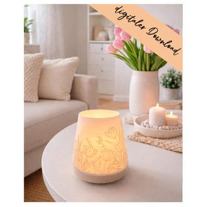Könnte beinhalten: Eine beleuchtete, cremefarbene Keramiklampe mit floralem Muster steht auf einem weißen Tisch. Eine Vase mit rosa Tulpen, brennende Kerzen und Kissen umgeben die Lampe. Der Text "digitaler Download" befindet sich oben rechts.