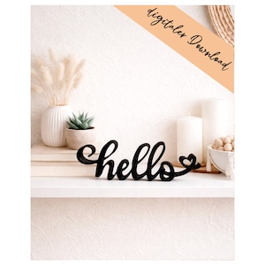 Puede incluir: Un letrero decorativo negro en letra cursiva que muestra la palabra hello con un pequeño corazón al final. El letrero está colocado sobre una superficie plana. Una banda naranja diagonal en la esquina superior derecha muestra el texto digitaler Download.