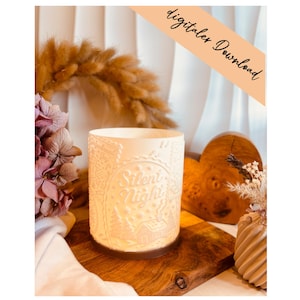 Może przedstawiać: Kremowy świecznik z napisem "Silent Night" i zimowym wzorem. Cylindryczny uchwyt stoi na drewnianej powierzchni, z suszonymi kwiatami i drewnianym sercem w tle. Słowa "digitaler Download" są napisane na ukośnym banerze.