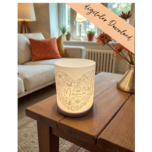 Könnte beinhalten: Eine weiße, zylindrische Lampe mit einem floralen Herzdesign und dem Wort "Mama" auf der Vorderseite. Die Lampe steht auf einem Holztisch in einem Wohnzimmer. Das Bild zeigt auch eine Vase mit Blumen und ein Sofa mit orangefarbenen Kissen. Der Text "digitaler Download" befindet sich oben rechts.