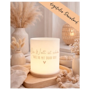 May include: A cylindrical white lamp with a light wood base, featuring the German text "Die Welt ist schön, weil du mit drauf bist" and a small heart symbol. The lamp emits a soft glow and is positioned on a wooden tray with wooden beads.
