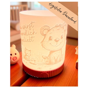 Può includere: Una luce notturna cilindrica illuminata, con una base rossa e una sezione superiore bianca. La sezione bianca presenta un disegno in rilievo di un orso, un gatto e un'anatra. È visibile anche il testo "du wirst endlich geliebt". Le parole "digitaler Download" sono scritte in diagonale.