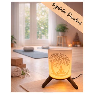 Könnte beinhalten: Zylindrische Lampe mit einem Baum- und Meditationsfigurendesign. Die Lampe hat einen weißen Schirm und steht auf einem dunkelbraunen Dreibein-Sockel. Das Bild enthält den Text "digitaler Download". Die Lampe steht auf einer hellbraunen Matte.