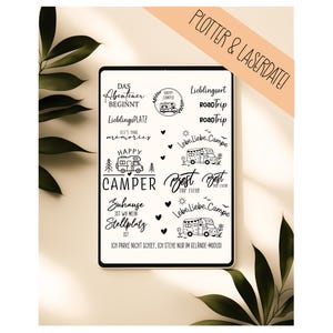 May include: A digital tablet screen displaying a collection of black graphic designs and text phrases related to camping and road trips, including phrases like Das Abenteuer beginnt, Happy Camper, and Lebe Liebe Campe, with camper van illustrations.