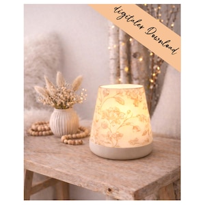 Pode incluir: Uma lâmpada acesa com padrão floral e base bege está sobre uma mesa de madeira. O design da lâmpada apresenta um fundo creme com um delicado padrão floral. Um pequeno vaso com flores secas e contas de madeira também está sobre a mesa. O texto "digitales Download" está na imagem.