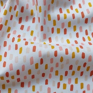 Könnte beinhalten: Weißer Stoff mit einem sich wiederholenden Muster aus vertikalen Pinselstrichen in Orange-, Gelb- und Rosatönen. Der Stoff ist leicht zerknittert, was auf ein weiches Material hindeutet. Das Design ist über die Oberfläche verstreut.