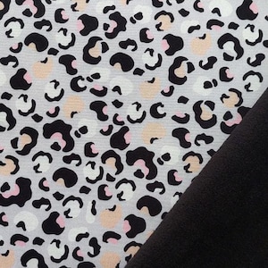 Könnte beinhalten: Nahaufnahme eines weißen Stoffes mit einem schwarzen und rosafarbenen Leopardenmuster. Der Stoff ist über einen schwarzen Stoff gefaltet.