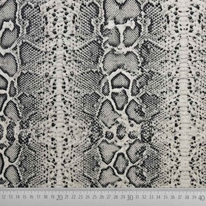 Może przedstawiać: Zbliżenie na tkaninę z czarno-białym wzorem skóry węża. Tkanina ma fakturowaną powierzchnię.