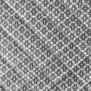 Op de afbeelding: Gewatteerde stof met een herhalend geometrisch patroon in grijstinten en wit. Het ontwerp bestaat uit verbonden vormen, waardoor een textuur ontstaat. De quiltlijnen vormen een ruitvormig raster over het oppervlak.