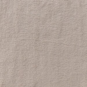 Könnte beinhalten: Nahaufnahme eines strukturierten, hellbeigen Stoffes. Das Material hat ein weiches, plüschiges Aussehen mit einem dichten, geschlungenen Flor. Die neutrale Farbe und die taktile Oberfläche deuten auf ein gemütliches, warmes Textil hin, das für Kleidung oder Heimdekoration geeignet ist.