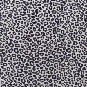 Può includere: Primo piano di un tessuto con un motivo a stampa leopardata ripetuto. Il motivo presenta macchie blu navy scuro su uno sfondo color crema. Le macchie variano per dimensioni e forma, creando un aspetto strutturato.