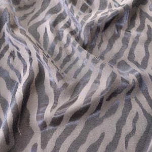 Pode incluir: Close-up de um tecido com padrão de listras de zebra. O tecido tem um fundo bege neutro com listras cinza escuro. O tecido está ligeiramente enrugado, criando sombras e destaques.