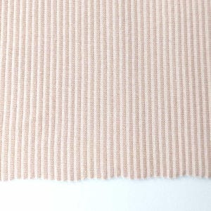 Può includere: Primo piano di una sezione di tessuto a maglia di colore beige chiaro. Il tessuto ha una trama a coste con linee verticali che vanno dall'alto verso il basso. Il bordo inferiore del tessuto è incompiuto, con un aspetto leggermente sfilacciato.