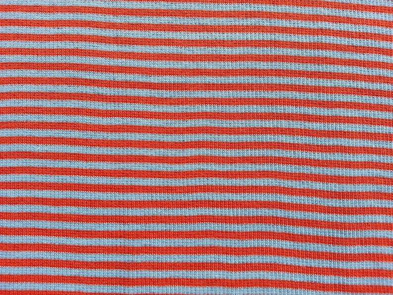 May include: A close-up of a fabric with alternating red and light blue stripes. The fabric has a textured, woven appearance.