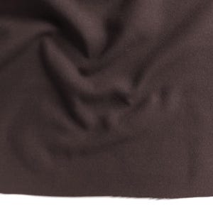 Könnte beinhalten: Nahaufnahme eines dunkelbraunen Stoffes mit weichem, strukturiertem Aussehen. Das Material weist subtile Falten und Schatten auf, die ein Gefühl von Tiefe und Dimension erzeugen. Der Stoff scheint einfarbig zu sein, geeignet für verschiedene Näh- und Bastelprojekte.