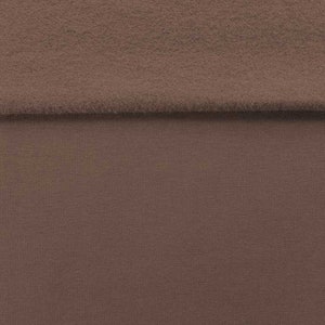 Op de afbeelding: Een close-up van een bruine stof met een textuur. De stof is dubbelgevouwen, waarbij de gladde kant aan de onderkant en de textuur aan de bovenkant zichtbaar is.