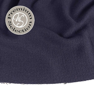 Könnte beinhalten: Nahaufnahme eines marineblauen Stoffes mit strukturierter Oberfläche. Ein kreisförmiges Emblem mit den Worten "Premium Selection" umgibt ein stilisiertes "WS"-Monogramm.
