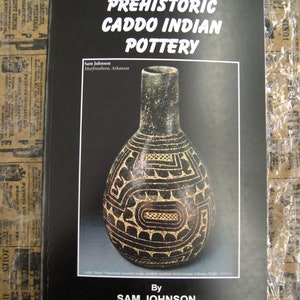 May include: A black and white book titled "Prehistoric Caddo Indian Pottery" by Sam Johnson. The book cover features a black and white ceramic pot with geometric designs.