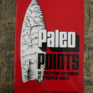 May include: A red book cover with the title "Paleo Points: An Illustrated Chronology of Projectile Points" and a black and white illustration of a spear point. The book is volume one and was compiled and illustrated by G. Bradford.