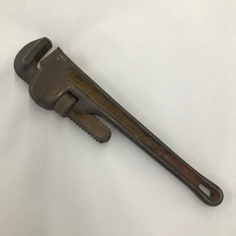 May include: A vintage pipe wrench, showing signs of age and use. The metal wrench has a long handle and adjustable jaws. The handle has a red painted section near the end. The wrench is designed for gripping and turning pipes. The overall length is approximately 30 cm.