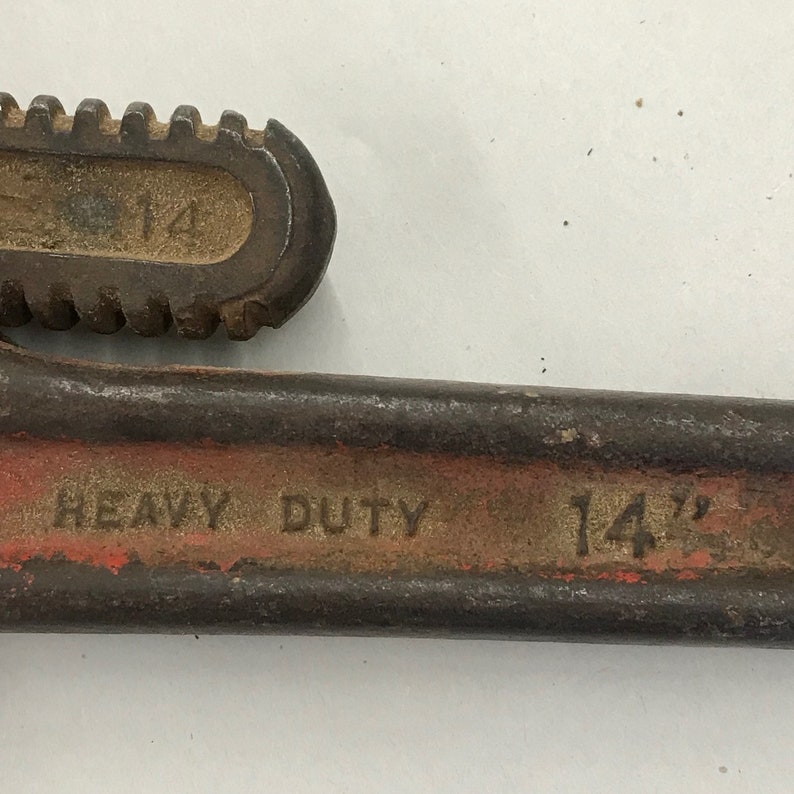 May include: Close-up of a heavy-duty pipe wrench. The wrench is primarily brown with red accents and the text "HEAVY DUTY" and "14"" printed on it. The adjustable jaw is also marked with the number "14".