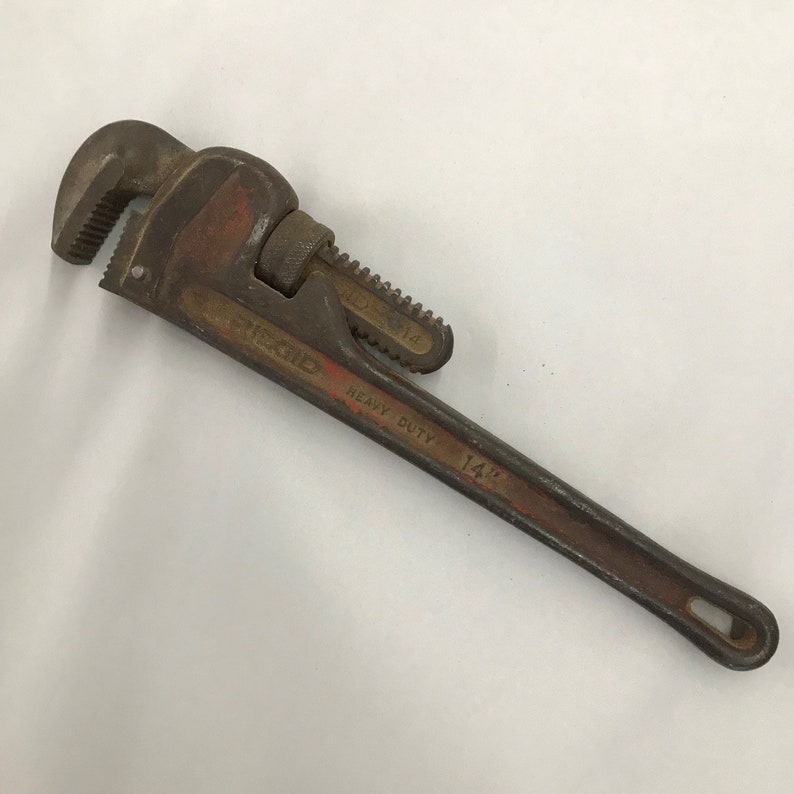 May include: A vintage 35.5 cm heavy-duty pipe wrench. The wrench is a rusty brown colour with red accents and the text "RIDGID HEAVY DUTY 14" printed on the handle. The jaws are serrated.
