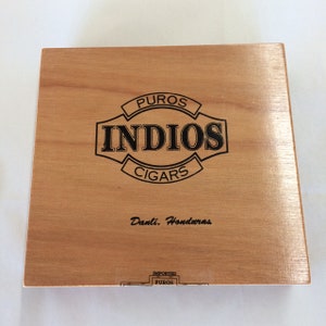 May include: A wooden box with a black and white logo that says "Puros Indios Cigars" and "Danli, Honduras". The box is labeled "Imported Puros".