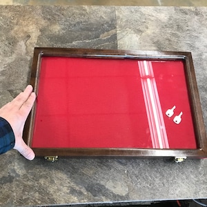 May include: A wooden display case with a red velvet interior and a glass top. Two small silver keys are visible inside the case.