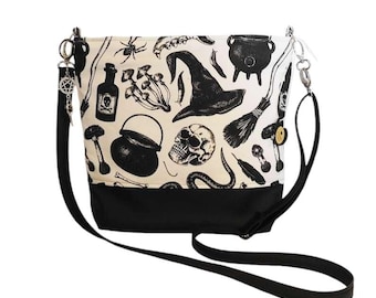 Pode incluir: Bolsa transversal preta e branca com estampa de bruxa assustadora. O design da bolsa inclui uma caveira, chapéu de bruxa, caldeirão e outras ilustrações. Possui base preta e alça longa e ajustável.