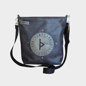 May include: A gray messenger bag with a black adjustable shoulder strap. The bag features a circular design with runes and a central symbol. The bag has a rectangular shape and a small tag that says "Darkside Designs".