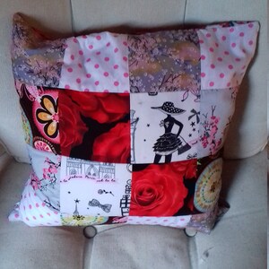 Puede incluir: Una almohada de patchwork con una variedad de patrones florales y geom&eacute;tricos en tonos de rosa, rojo, blanco y negro. La almohada est&aacute; hecha de cuadrados de tela cosidos juntos para crear un dise&ntilde;o &uacute;nico.