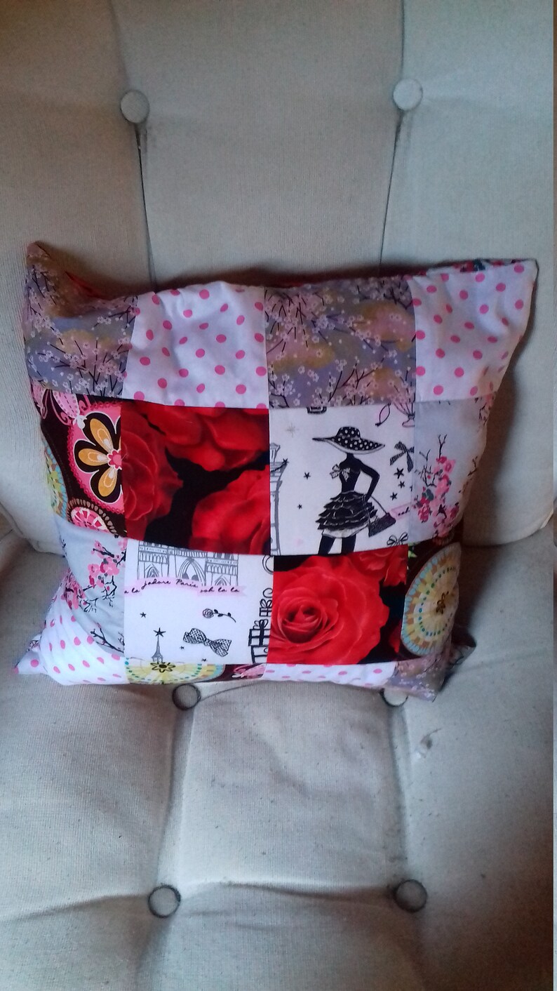 Puede incluir: Una almohada de patchwork con una variedad de patrones florales y geom&eacute;tricos en tonos de rosa, rojo, blanco y negro. La almohada est&aacute; hecha de cuadrados de tela cosidos juntos para crear un dise&ntilde;o &uacute;nico.