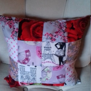 Peut inclure: Un coussin patchwork avec une variété de motifs, dont une rose rouge, un motif floral rose, une tour Eiffel noire et blanche et un bâtiment blanc avec une tour d'horloge. Le coussin est en tissu et a un fond blanc.
